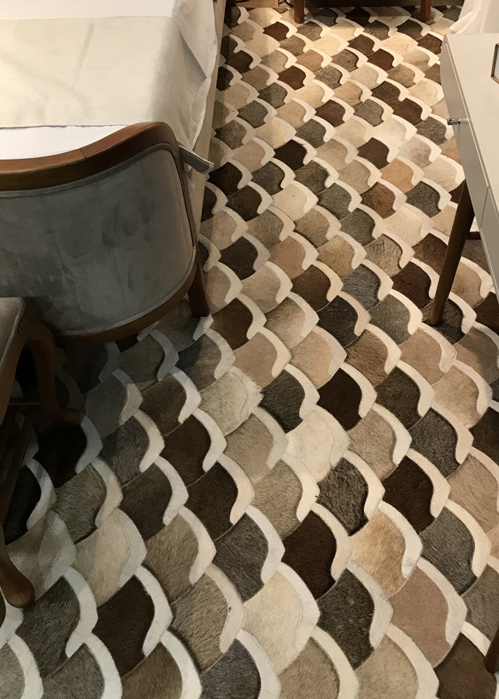 A cowhide patchwork rug with a geometric pattern in black, brown, beige, and white colors, laid out on a floor.