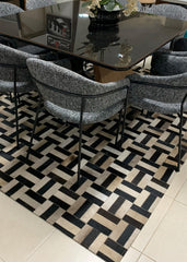 A beige and black patchwork cowhide rug laid out on a floor, with a dining table and chairs set on top of it.