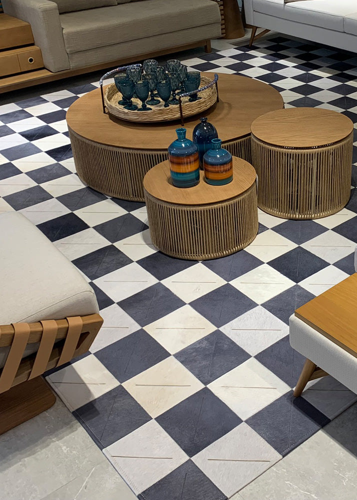 A two-tone cowhide patchwork rug featuring a black and brown color scheme, placed on a herringbone patterned floor, with a round shape and a flat base, surrounded by a variety of decorative items.