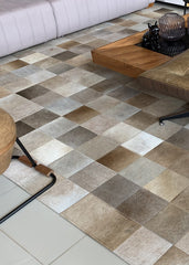 A cowhide patchwork rug featuring a geometric pattern in beige and gray tones, laid out on a tiled floor in a living room setting.