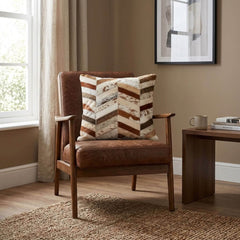 Brown and ivory cowhide patchwork cushion with chevron design styled on a tan leather armchair