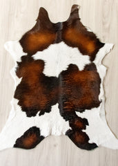 Brown, black, and white calfskin hide rug on a wooden floor.