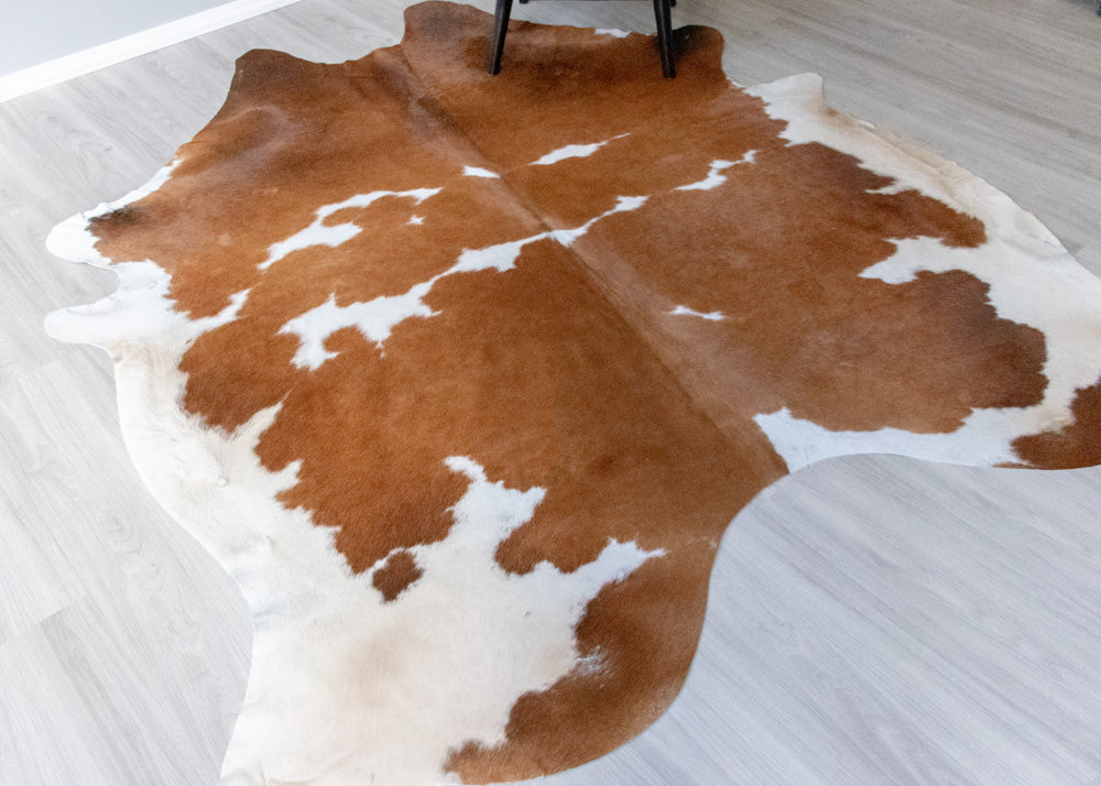 Brown and white cowhide rug on a light wooden floor