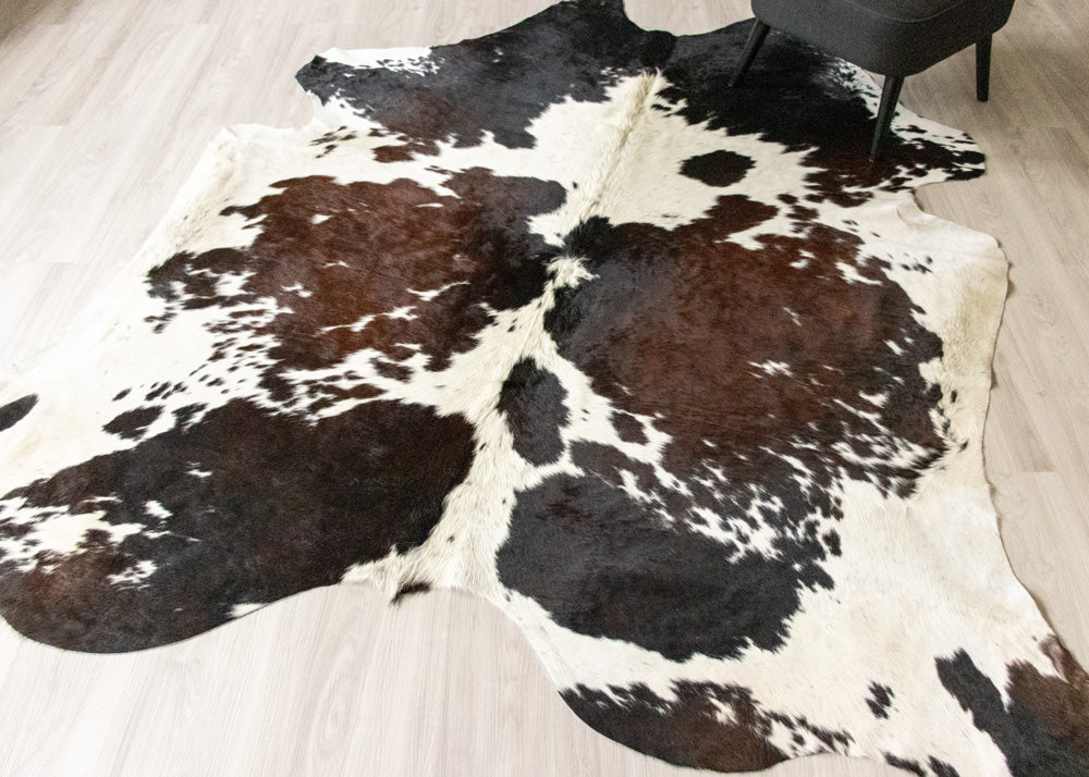 Cowhide rug with reddish, black, white and brown on a light wooden floor.