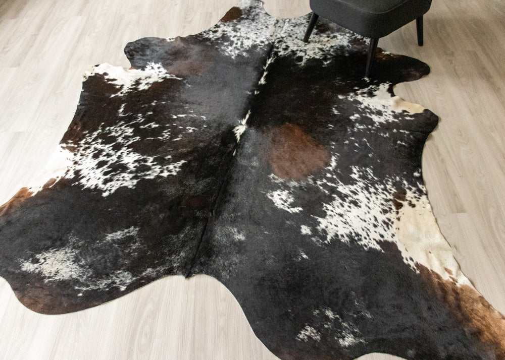 Brown and white tricolor cowhide rug on a wooden floor