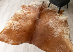 Brown and white cowhide rug on a light wooden floor