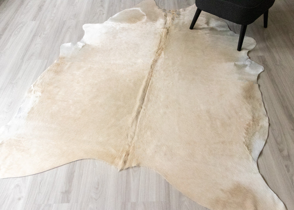 Champagne Beige cowhide rug on a wooden floor with a black chair