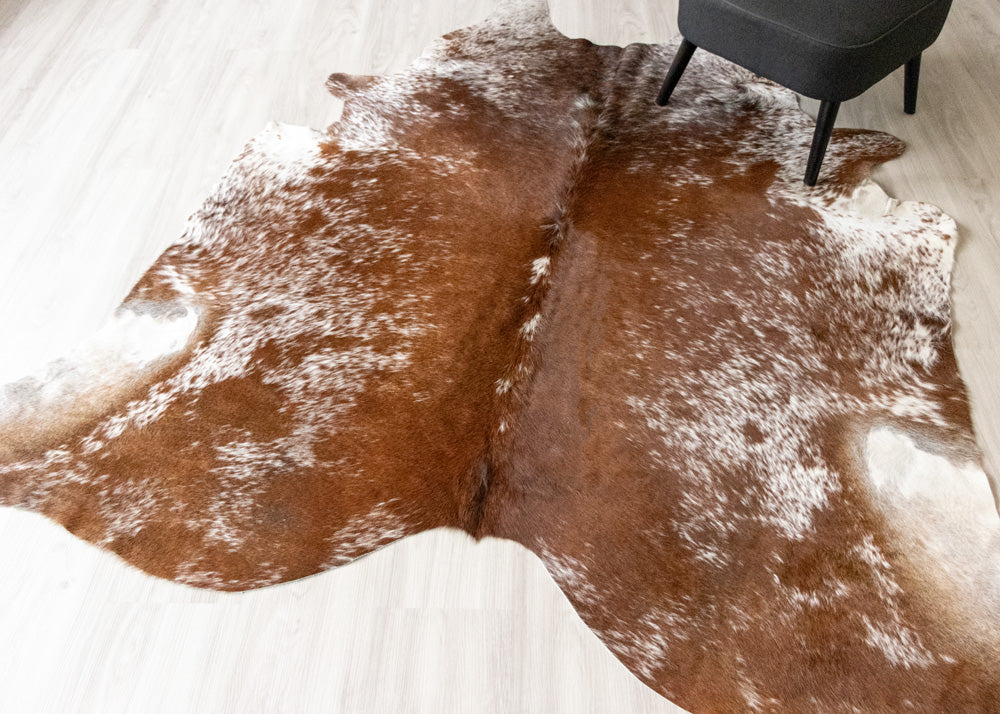 Brown and white cowhide rug on a light wooden floor