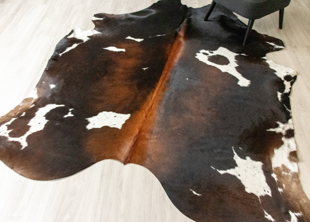 Cowhide rug with black, brown, and white pattern on a light wooden floor.
