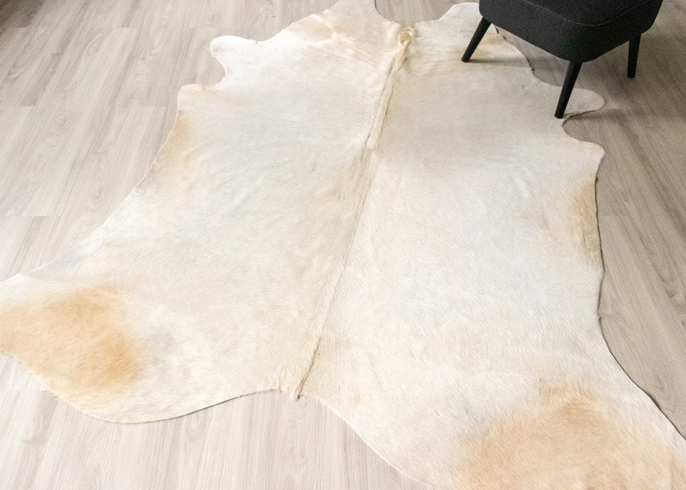 White champagne cowhide rug with brown on a light wooden floor.