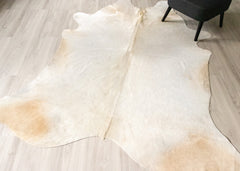 White champagne cowhide rug with brown on a light wooden floor.