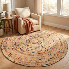 Round multicolored jute rug on a wooden floor with a chair and lamp in the background.