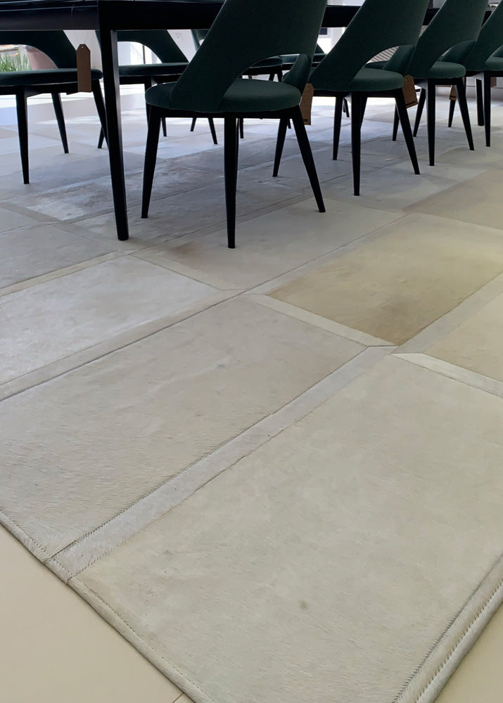 An off-white cowhide patchwork rug laid out on a tiled floor with furniture set on top of it.