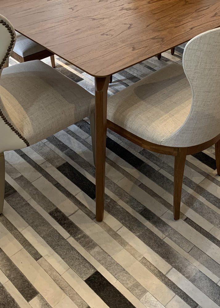 A cowhide patchwork rug with a geometric pattern in gray tones, laid out on a floor with furniture on top of it.