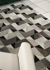 A cowhide patchwork rug with a geometric pattern in gray, black, and white colors, laid out on the floor.