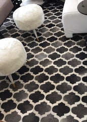 A cowhide patchwork rug with a geometric pattern in gray and white colors, with a dotted pattern on the gray side and a flat surface on the white side.