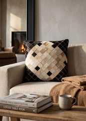Black and ivory cowhide patchwork cushion with diamond design styled on a neutral armchair