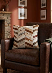 Brown and ivory chevron cowhide patchwork cushion styled on a dark brown leather armchair