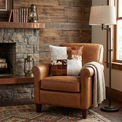 Brown and white cowhide patchwork cushion on a tan leather armchair in a rustic living room