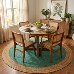 Dining room with wooden table and chairs on a round green jute rug, plants, and a cabinet.