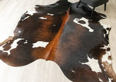 Cowhide rug with black, brown, and white pattern on a light wooden floor.