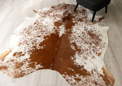Brown and white cowhide rug on a light wooden floor with a black stool.