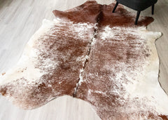 Brown and white cowhide rug on a light wooden floor.