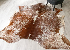 Brown and white cowhide rug on a light wooden floor.