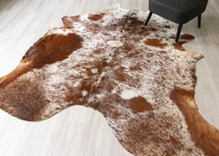 Brown and white cowhide rug on a light wooden floor with a chair in the corner.