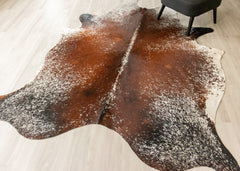Brown and white cowhide rug on a light wooden floor