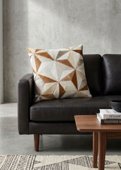 Tan and ivory faceted cowhide patchwork cushion styled on a black leather sofa